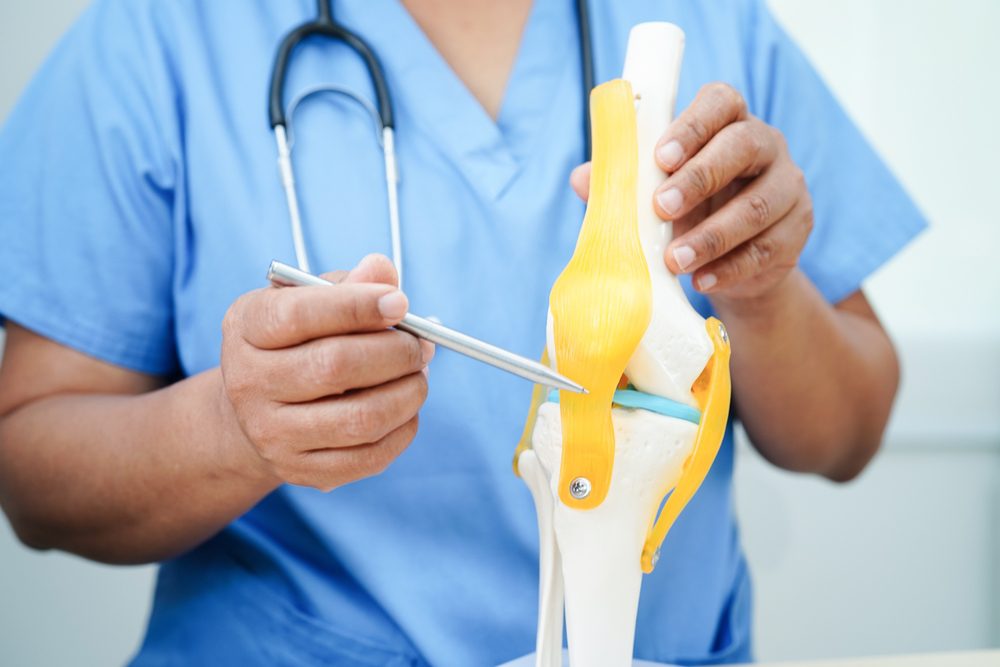 Doctor explaining how osteoarthritis pain in the knee is caused using a model of a knee