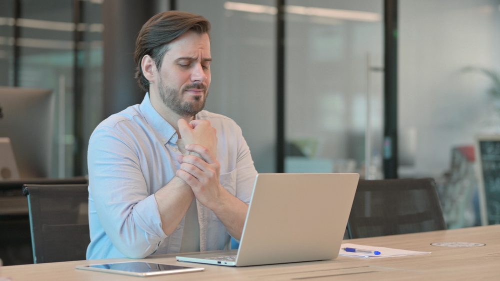 man with wrist pain. Worker at desk suffering from pain in the wrist.